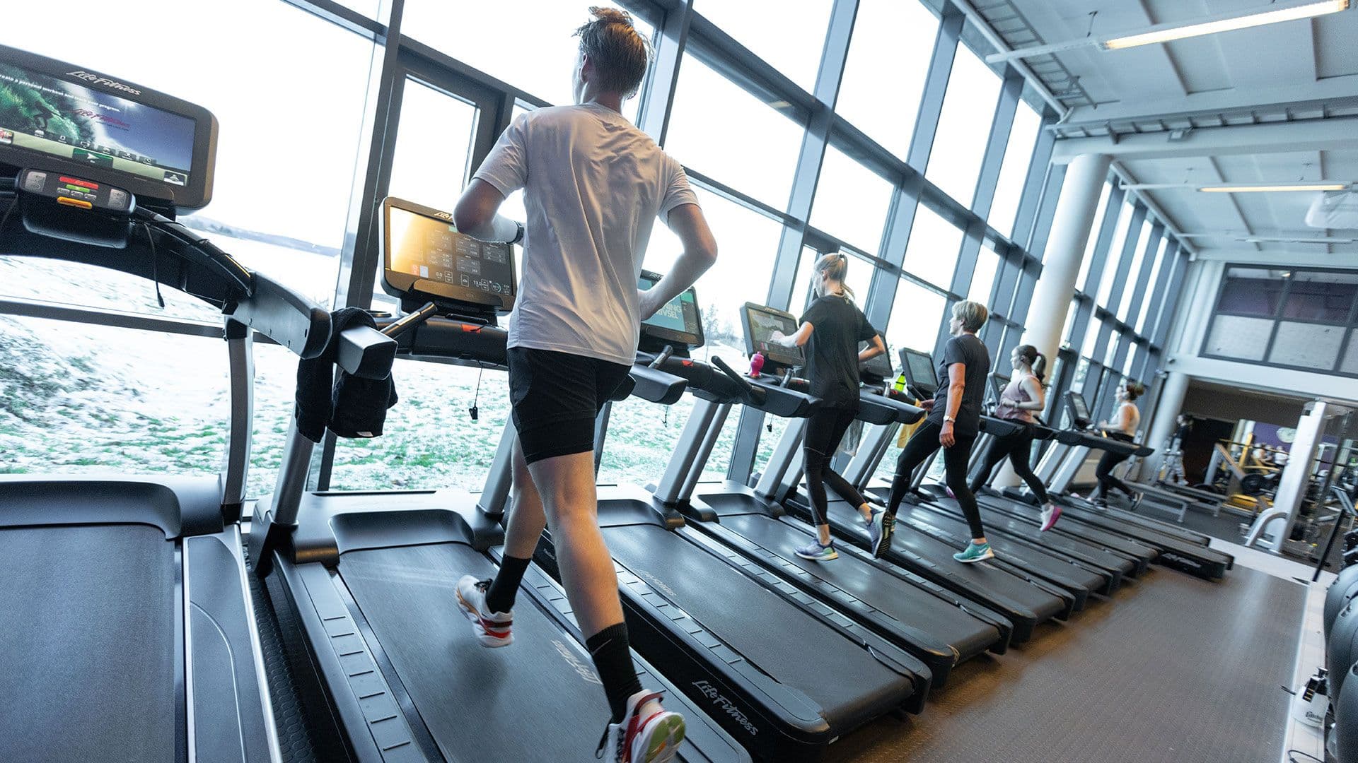 Ung mann løper på tredemølle foran panoramavinduene i treningssalen på 3T-Levanger.