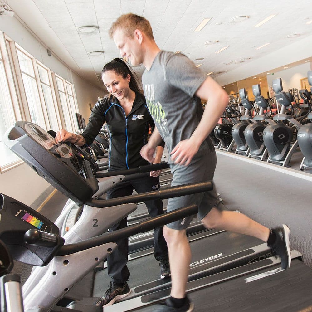 Mann løper på tredemølle, med personlig trener som backer.