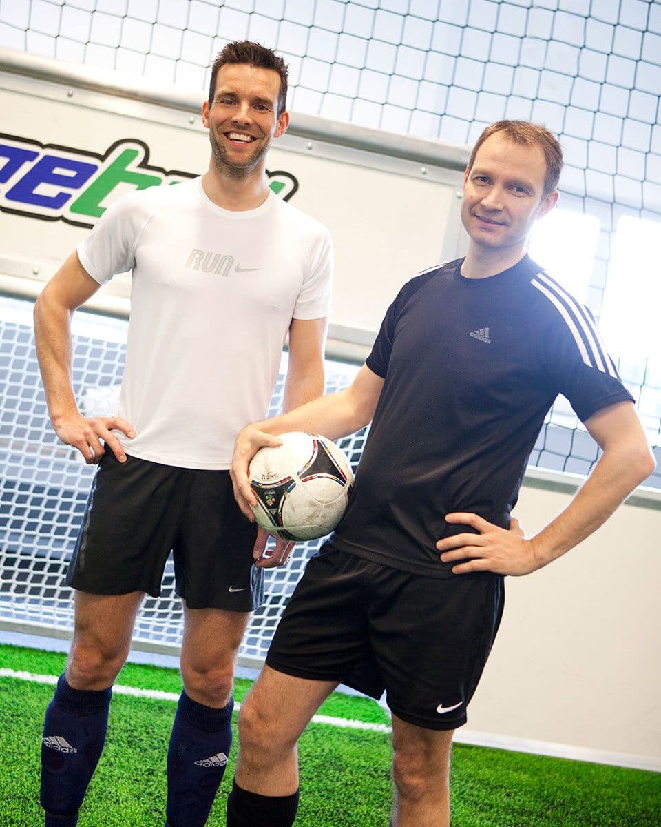 To menn står poserer med fotball, inne i Cageball Rosten.